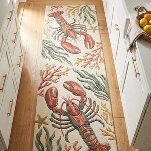 May include: A rectangular runner rug featuring a cream-coloured background with a repeating pattern of red lobsters, green seaweed, yellow coral, and small starfish. The design is oriented vertically, showcasing marine life in a textured finish.