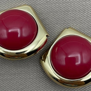 Op de afbeelding: Een paar gouden oorbellen met grote, ronde, felroze cabochons.