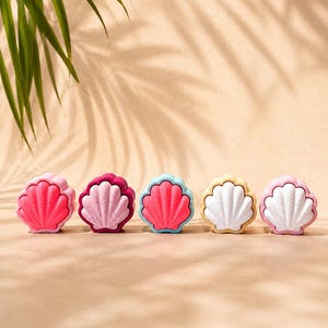 May include: Five shell-shaped hair brushes arranged in a row. Each brush features a two-tone design with a textured, scalloped outer shell and a contrasting inner bristle pad. The colors include pink, magenta, light blue, yellow, and white.