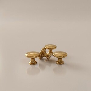 Peut inclure: Un ensemble de quatre petits boutons de placard ronds en métal doré. Chaque bouton présente une surface lisse et polie avec un dessus circulaire et une base effilée qui se connecte à une tige centrale, conçus pour les meubles.
