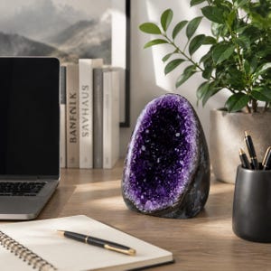 Op de afbeelding: Een grote, eivormige amethist-geode met een dieppaarse, kristallijne binnenkant en een donkere, natuurlijke stenen buitenkant. De geode staat rechtop en toont de grillige, sprankelende kristalformatie in het holle midden.