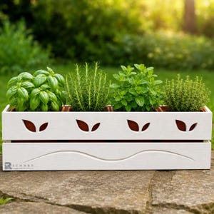 Peut inclure: Une jardinière rectangulaire en bois blanc contenant quatre pots en terre cuite avec des herbes vertes. La façade présente des découpes en forme de feuilles et une ligne horizontale ondulée, avec la marque Richard Fine Wood imprimée.