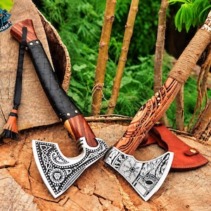 May include: Two hand axes with metal heads featuring intricate silver-toned engravings of Norse patterns and symbols. The left axe has a black leather-wrapped handle with a tassel, while the right axe features a carved wooden handle with rope wrapping.