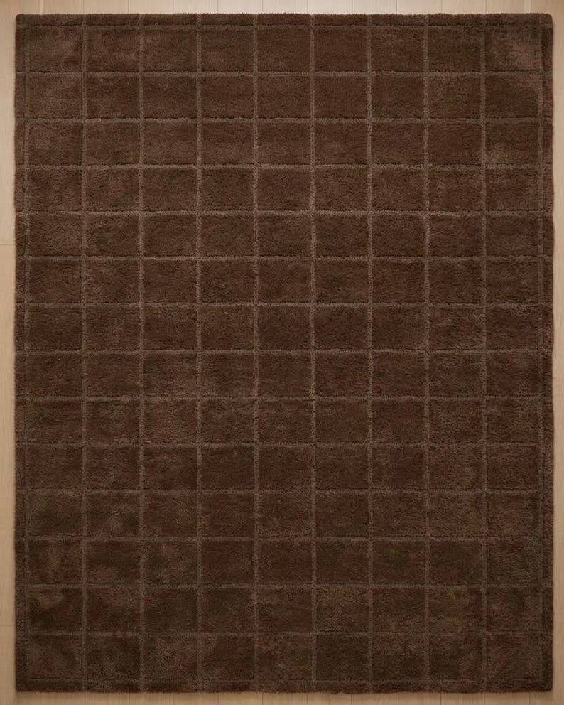 May include: A rectangular area rug in a solid dark brown color featuring a uniform grid pattern of raised square tufts. The surface texture is consistent throughout, creating a repeating geometric design across the entire floor covering.