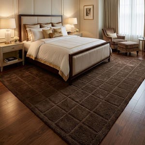 May include: A large, rectangular, dark brown area rug with a grid-like, tufted square pattern covering the entire surface. The rug is placed on a wooden floor in a bedroom, featuring a dark wood bed frame, white bedding, and two bedside lamps.