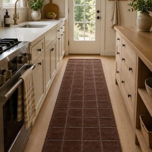 A kitchen runner rug with a brown geometric pattern extends down a narrow kitchen aisle between white cabinets and a wooden island.