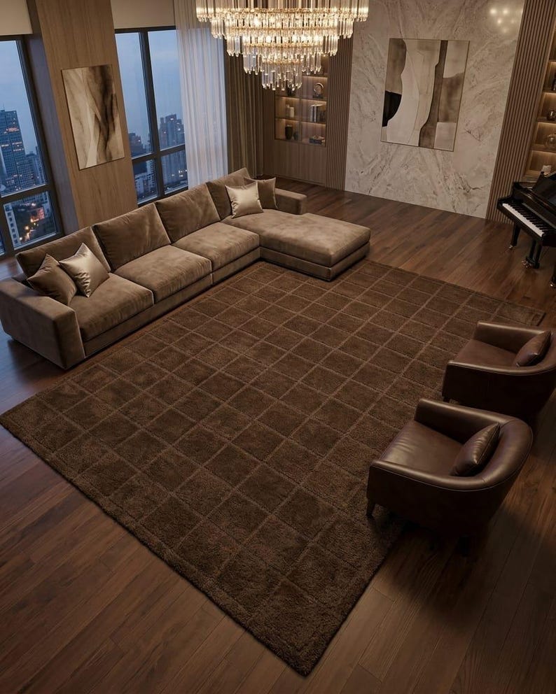 May include: A large, rectangular, dark brown area rug featuring a grid pattern of recessed squares. The rug is positioned on a dark wood floor in a living room setting, surrounded by a brown sectional sofa, two leather armchairs, and a grand piano.
