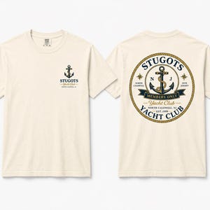 May include: A cream-colored short-sleeve t-shirt featuring a small anchor logo on the left chest and a large circular graphic on the back. The back design includes a rope border, an anchor, and the text STUGOTS YACHT CLUB MEMBERS ONLY.