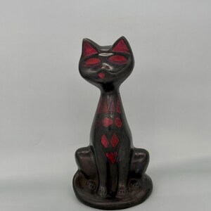 May include: Black ceramic cat figurine with red geometric designs. The cat is sitting with its tail curled around its legs.