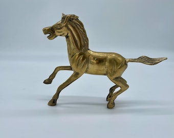 May include: A solid brass horse figurine with a detailed mane and tail. The horse is in a running pose with its head turned to the side.