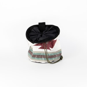 May include: A white and red patterned drawstring bag with a black top and a green drawstring. The bag is made of a soft, durable fabric and is perfect for carrying small items.