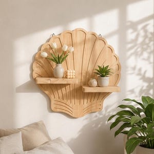 Puede incluir: Un estante de pared de madera clara con forma de concha grande y dos niveles horizontales. El estante superior sostiene un pequeño jarrón con tulipanes blancos y una vela cuadrada, mientras que el inferior sostiene un cuenco pequeño y una suculenta verde.