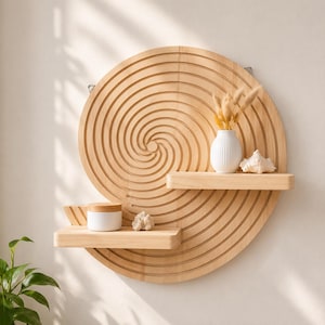 May include: A circular light-colored wooden wall shelf featuring a carved spiral pattern. The unit includes two horizontal shelves holding a white vase with dried grasses, a small white jar with a wooden lid, and two small white decorative stones.