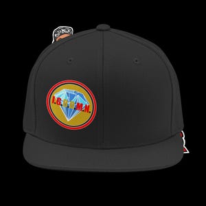 May include: A black baseball cap featuring a circular patch on the front. The patch has a gold background, a red border, and a blue diamond graphic with the red text I.G.B.B.M.N. printed across it. A small cartoon figure is visible behind the cap.