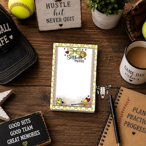 May include: A rectangular notepad featuring a softball-themed border with yellow softballs, red hearts, and stars. The top centre displays a green bow, a softball glove, and the text "Softball MAMA". The bottom includes a softball bat and hearts.
