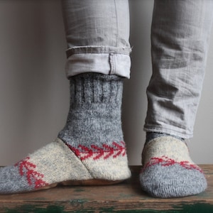 May include: A pair of gray wool socks with red and white knit patterns. The socks are folded down at the ankle and are worn with gray jeans.