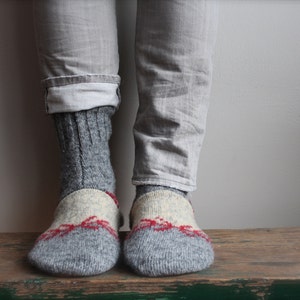 May include: A pair of gray wool socks with red and white accents. The socks are folded down at the top, revealing the gray wool fabric.