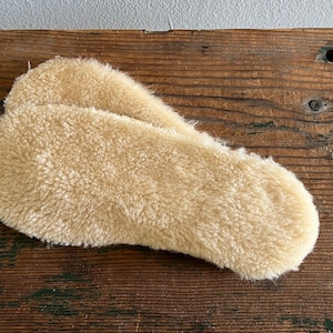 May include: Two beige sheepskin insoles for shoes or boots. The insoles are made of soft, fluffy sheepskin and are designed to provide warmth and comfort.