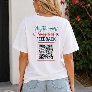 Può includere: Una t-shirt bianca a maniche corte con la scritta My Therapist Suggested FEEDBACK in verde acqua, rosa e blu scuro, accompagnata da due piccoli cuori rosa e un grande codice QR in bianco e nero incorniciato da un sottile quadrato rosso sul retro.