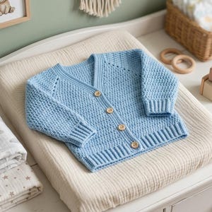 Può includere: Un cardigan a maniche lunghe color azzurro con un motivo a maglia testurizzato, scollo a V e quattro bottoni in legno marrone chiaro sul davanti. Il capo presenta polsini e orlo a coste, caratterizzato da una costruzione classica per neonati.