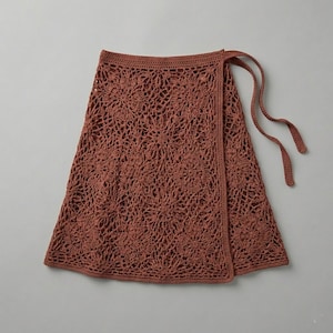 Peut inclure: Une jupe portefeuille en crochet de couleur rouille présentant un motif floral complexe sur tout le tissu. Le vêtement comprend une ceinture solide et deux longs liens en crochet assortis s'étendant sur le côté pour une fermeture.
