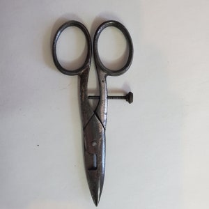May include: A vintage pair of metal scissors with a silver finish. The scissors have a single screw in the center and a pointed tip.