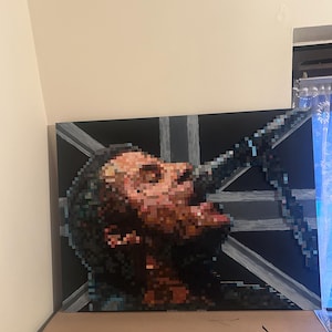 May include: A rectangular canvas painting featuring a pixelated portrait of a person looking upward. The artwork uses a palette of brown, black, and grey tones, set against a background with a stylized grey cross pattern on a solid black field.