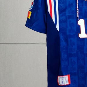 May include: A blue soccer jersey featuring a white collar with red and blue stripes, a white number 1 on the chest, and a repeating FFF logo pattern. The sleeve has a circular emblem and a small rectangular patch with the text FFF and a rooster icon.