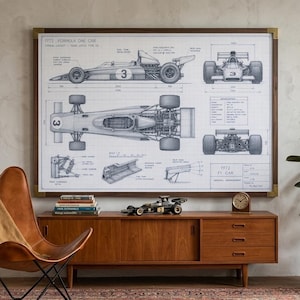 May include: A large framed technical blueprint print of a 1972 Formula One car, featuring side, top, front, and rear views with detailed annotations and measurements. The artwork is displayed in a dark wood frame with gold-toned corner accents.