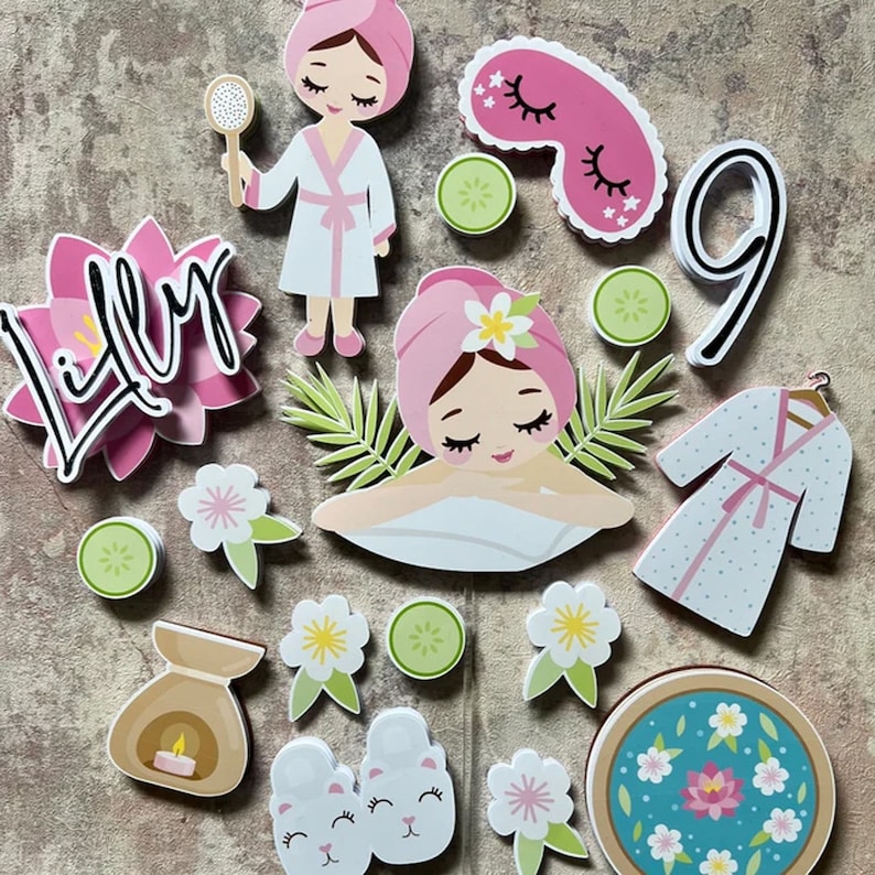 May include: A set of pink and white spa-themed cake toppers featuring a girl in a robe, a girl getting a facial, a lotus flower, a cucumber, a bathrobe, slippers, a candle, and the number 9. The name "Lily" is written on a pink lotus flower.