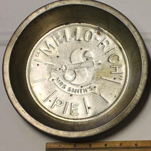 May include: A silver pie pan with the words "Mello-Rich Mrs. Smith's Pie" embossed on the bottom. The pan has a decorative design of a rolling pin and a pie crust.
