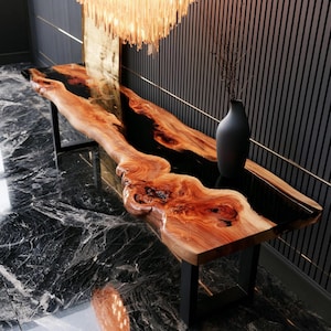 Può includere: Un lungo tavolo console caratterizzato da un piano in legno naturale a bordo vivo con venature e nodi prominenti, integrato con una sezione centrale in resina nera liscia. Il tavolo è sostenuto da gambe in metallo nero e un vaso nero opaco.