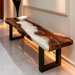 Puede incluir: Una mesa consola larga con un tablero de madera de borde natural y un río central de resina blanca translúcida. La mesa se apoya sobre dos patas rectangulares de metal negro y muestra un patrón de veta de madera natural en tonos marrones.