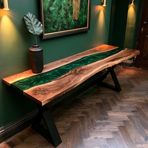 May include: A rectangular console table featuring a live-edge walnut wood top with a central river inlay made of translucent emerald green resin. The table is supported by a black metal base with angled legs and a matte finish.