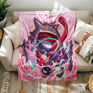 May include: A rectangular fleece blanket featuring a vibrant graphic print of three purple ghost-like creatures in various sizes. The design includes swirling pink smoke, a long red tongue, and glowing teal energy accents against a soft pink background.