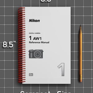 May include: A white Nikon 1 AW1 digital camera reference manual with a red spiral binding. The cover features black text, a camera illustration, and the number 1. Dimensions are 5.5 inches by 8.5 inches, shown next to a yellow pencil.