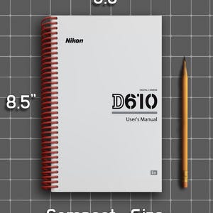 May include: A white Nikon D610 digital camera user's manual with a red spiral binding. The cover features the text Nikon, D610, Digital Camera, User's Manual, and En. The manual measures 5.5 inches by 8.5 inches, shown next to a yellow pencil.