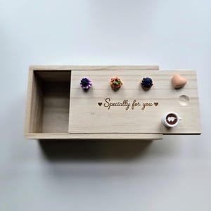 Puede incluir: Una caja deslizante de madera clara con el texto grabado "Specially for you" flanqueado por dos corazones pequeños. En la tapa hay objetos decorativos en miniatura: una mora, una pequeña tarta, un arándano, un corazón y una taza de café.