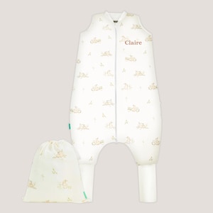 May include: A white sleeveless wearable blanket with a central zipper and leg openings, featuring a repeating pattern of small brown rabbits and foliage. The name Claire is embroidered in brown text on the upper chest, accompanied by a matching drawstring bag.