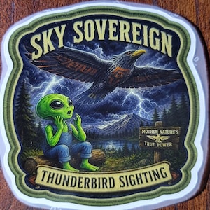 May include: A die-cut sticker featuring a green alien sitting on a log, looking up at a large dark bird flying through a stormy sky with lightning. The text reads SKY SOVEREIGN at the top, THUNDERBIRD SIGHTING at the bottom, and MOTHER NATURE'S TRUE POWER.