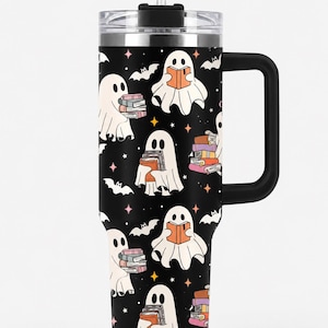 May include: A black stainless steel tumbler with a handle and a clear lid featuring a straw. The exterior is decorated with a repeating pattern of white ghosts holding colorful books, small black bats, and tiny orange and pink four-pointed stars.
