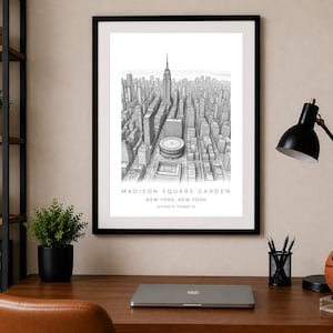 May include: A black and white architectural print in a black frame featuring a detailed bird's-eye view of New York City, including Madison Square Garden. The text reads MADISON SQUARE GARDEN, NEW YORK, NEW YORK, and the coordinates 40.7505° N, 73.9934° W.