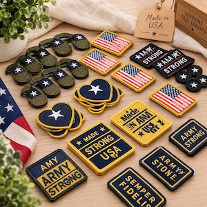 May include: A collection of embroidered patches featuring American flag rectangles, heart-shaped patches with white stars, and rectangular patches with text including ARMY STRONG, MADE IN USA, and SEMPER FIDELIS, all with yellow borders.