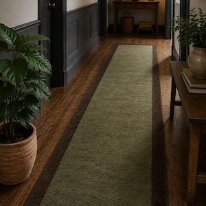 May include: A long rectangular runner rug featuring a textured olive green centre panel framed by a solid dark brown border. The rug is positioned lengthwise on a dark wood floor, showcasing a simple two-tone design with a plush, soft pile surface.