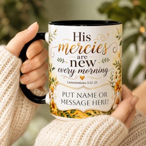 May include: A white ceramic mug with a black handle and interior, featuring a floral design in yellow and green. The text reads: His mercies are new every morning, Lamentations 3:22-23, and a placeholder box with the text: PUT NAME OR MESSAGE HERE!