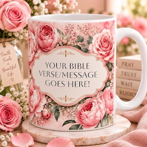 May include: A white ceramic mug featuring a floral pattern of pink roses and small white flowers. In the center, a decorative scalloped frame contains the black text: YOUR BIBLE VERSE/MESSAGE GOES HERE! The mug has a curved handle and a smooth finish.