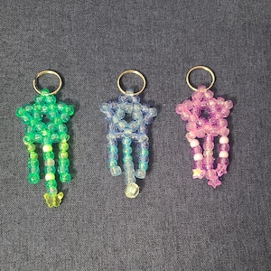 May include: Three star-shaped charms made of translucent plastic beads, each attached to a silver-tone metal ring. The charms are green with a yellow butterfly, light blue with a clear bead, and pink with small star-shaped beads at the ends.