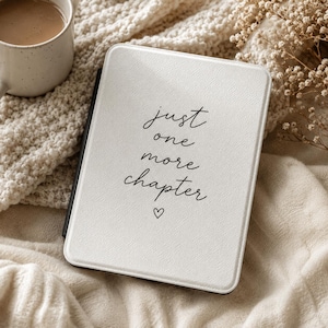 May include: A white e-reader case with a textured finish featuring the black printed text "just one more chapter" and a small heart icon centered below the words. The case has a slim profile and rounded corners, providing a clean look.