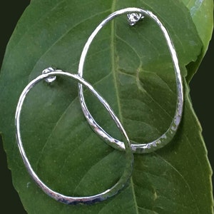 May include: A pair of silver hoop earrings with a hammered texture. The earrings are oval shaped and have a smooth, polished finish.