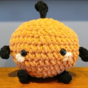 Può includere: Un peluche rotondo lavorato all'uncinetto con filato arancione morbido e testurizzato. Presenta due occhi in plastica nera lucida, piccoli accenti in filato bianco sotto gli occhi e appendici in filato nero, inclusi due bracci, due piedi e un germoglio.